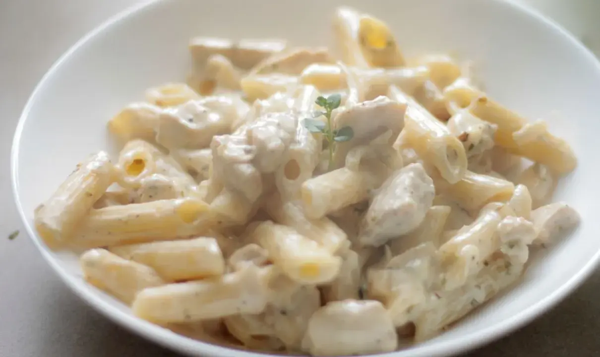 Penne z kurczakiem w kremowym sosie, udekorowane gałązką ziół. Pyszne danie, które zachwyci każdego smakosza.