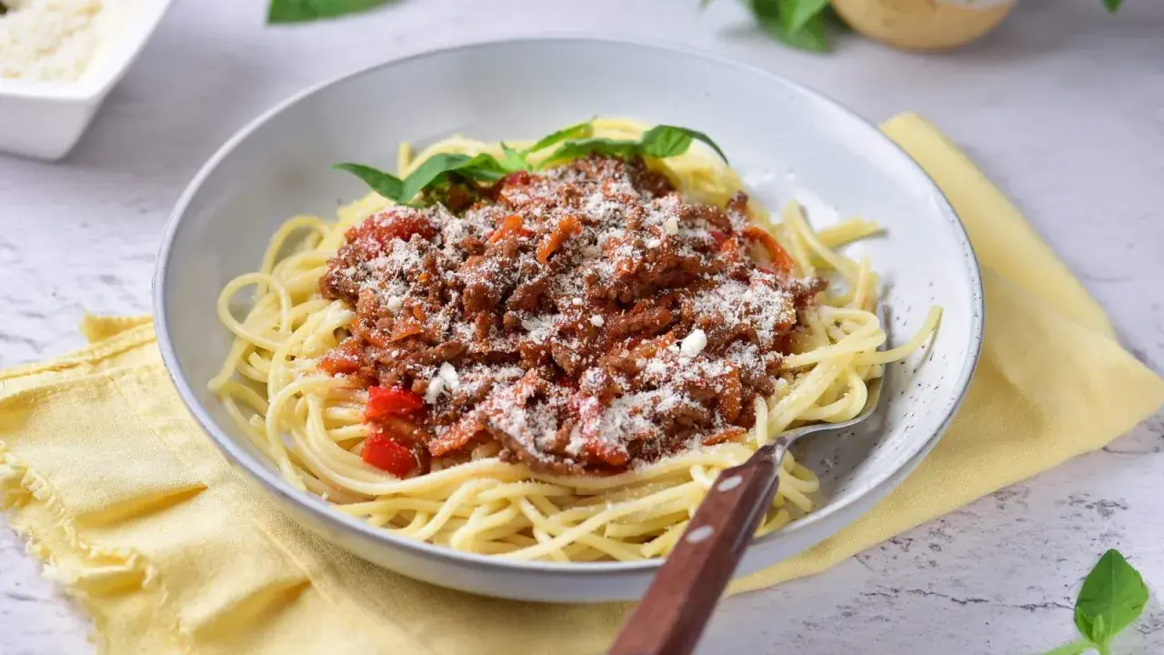 Pyszne spaghetti z bogatym sosem mięsnym na bazie passaty, posypane parmezanem i udekorowane listkami bazylii.