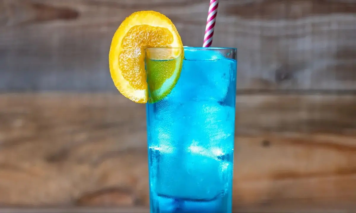 Orzeźwiający drink z blue curacao, ozdobiony plasterkiem pomarańczy i limonki, z kolorową słomką. Idealny na letnie popołudnie.