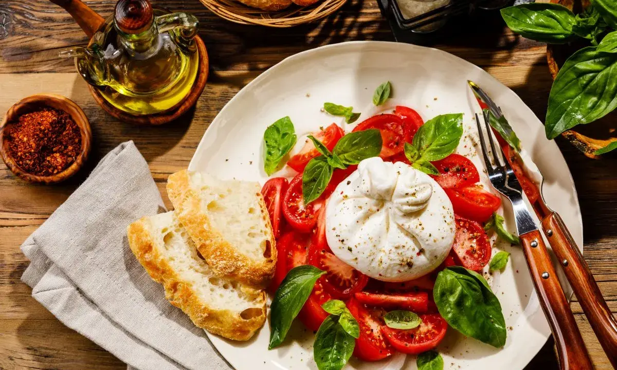 Pyszna burrata z pomidorami i bazylią, podana z chrupiącym pieczywem. To jest właśnie burrata – ser, który rozpływa się w ustach!