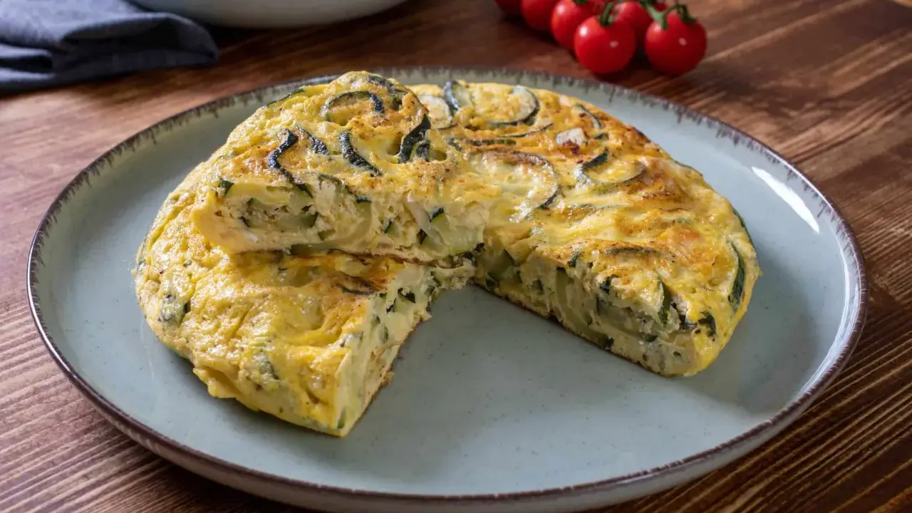 Pyszna frittata z cukinią, podana na talerzu, z pomidorkami koktajlowymi w tle.