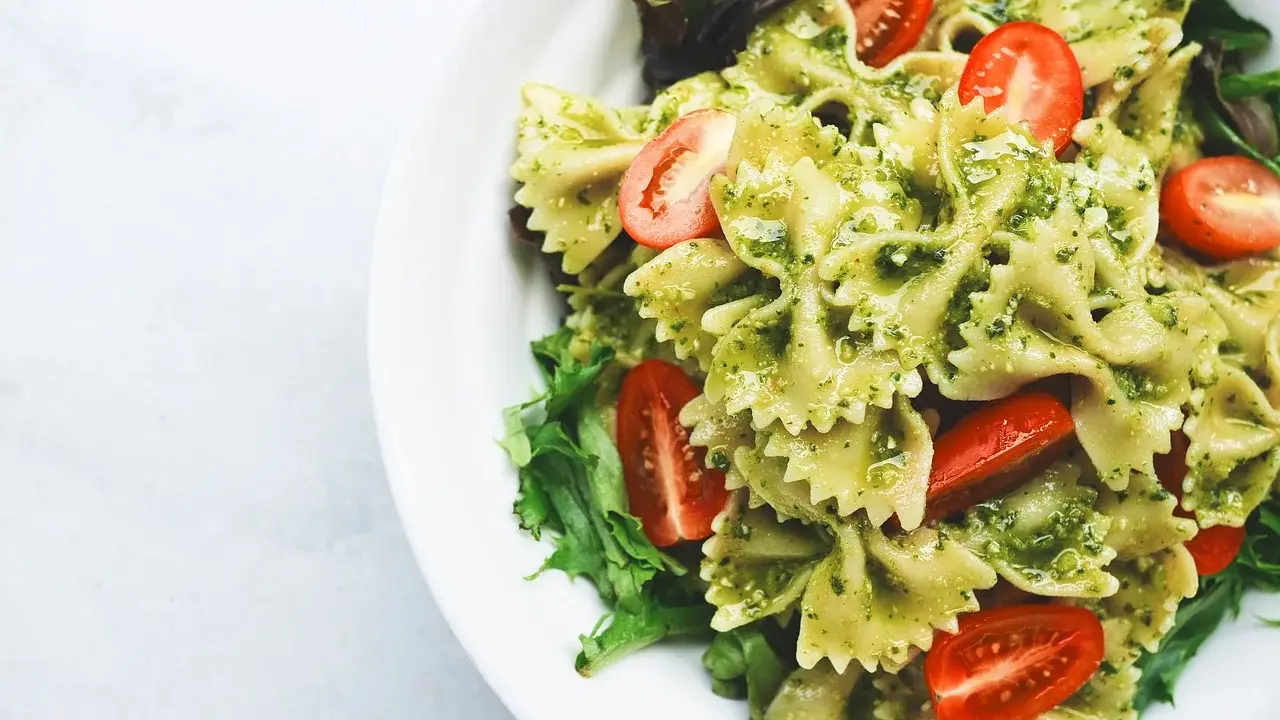 Makaron farfalle z zielonym pesto ze słoika, udekorowany połówkami pomidorków koktajlowych i listkami sałaty.