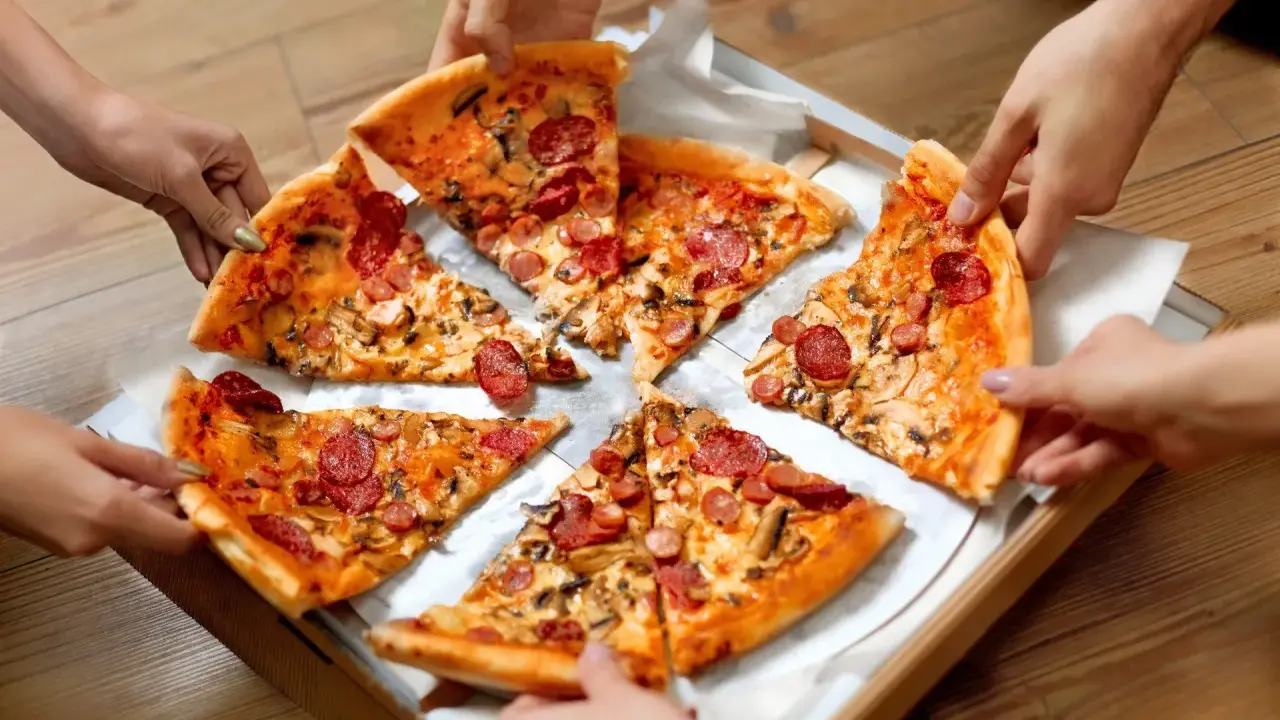 Ręce sięgają po kawałki pysznego ciasta na pizzę z kiełbasą i grzybami.
