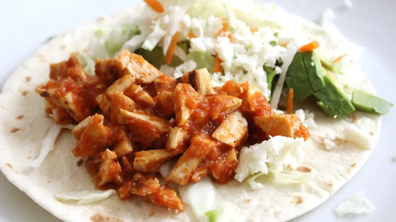 Pyszna tortilla z kurczakiem w sosie, posypana serem feta, z dodatkiem świeżej sałaty i awokado.