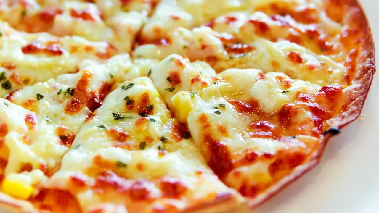 Pyszna pizza z tortilli, obficie posypana serem i ziołami, pokrojona na trójkątne kawałki.