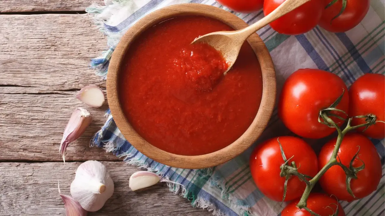 Domowy sos do pizzy z koncentratu, czosnek i świeże pomidory na drewnianym blacie.