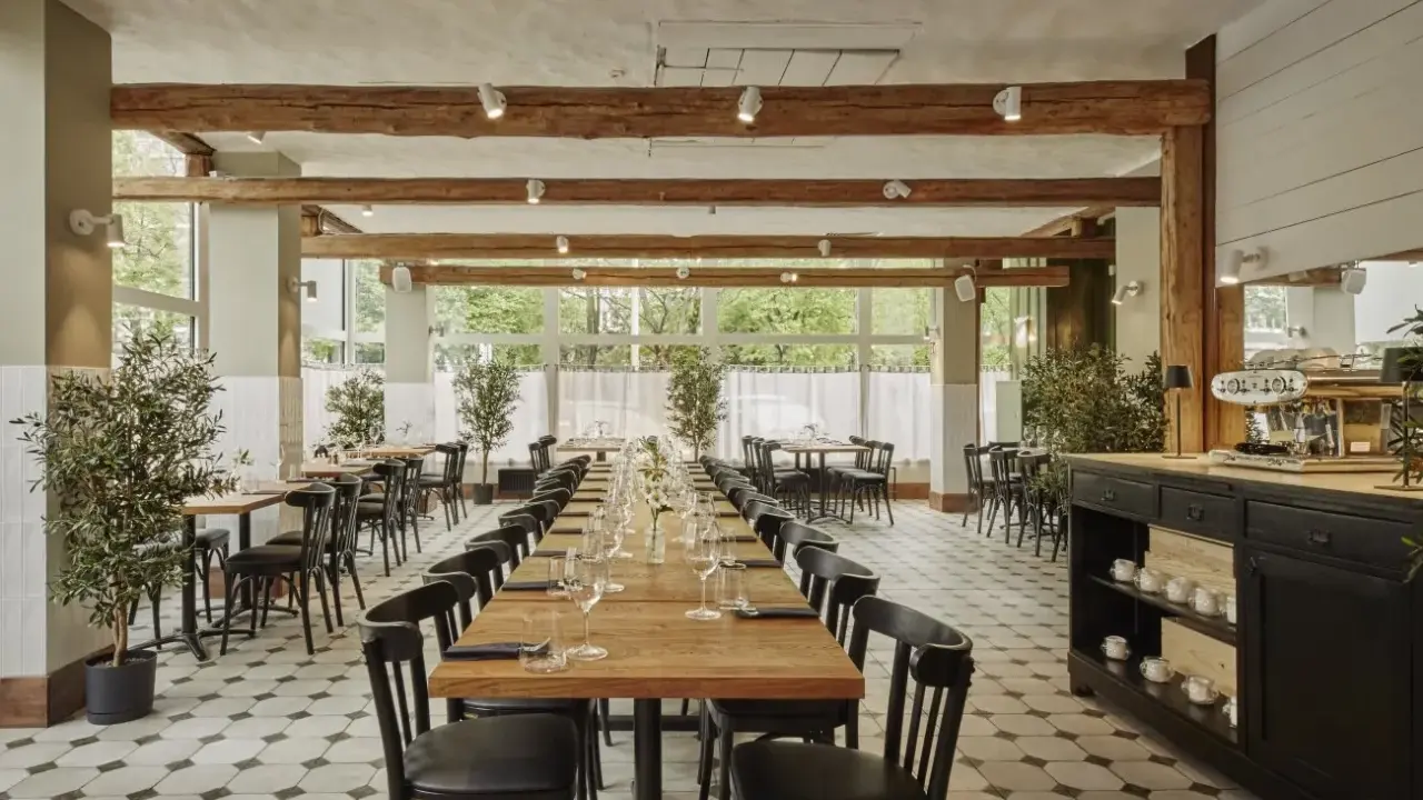 Elegancka sala restauracyjna z długimi stołami, idealna na degustację **primitivo kuchnia i wino**. Drewniane belki i duże okna tworzą przytulną atmosferę.