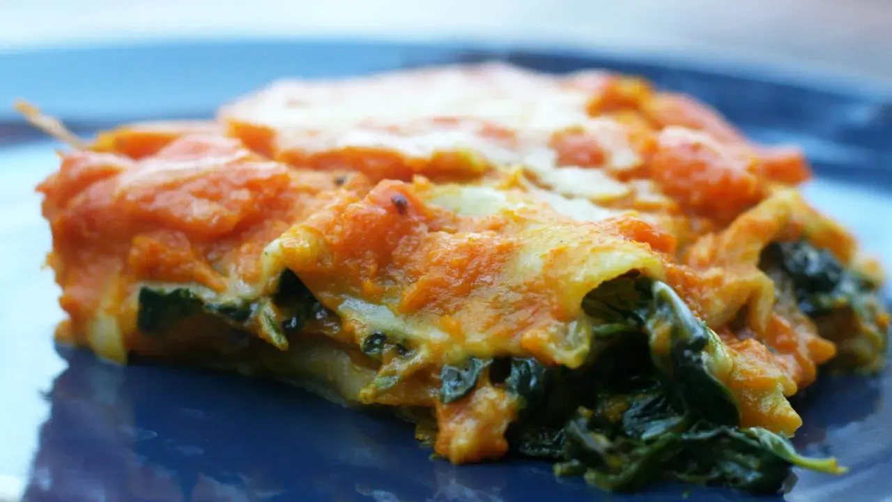 Pyszne lasagne ze szpinakiem, z pomarańczowym sosem i ciągnącym się serem, na granatowym talerzu.