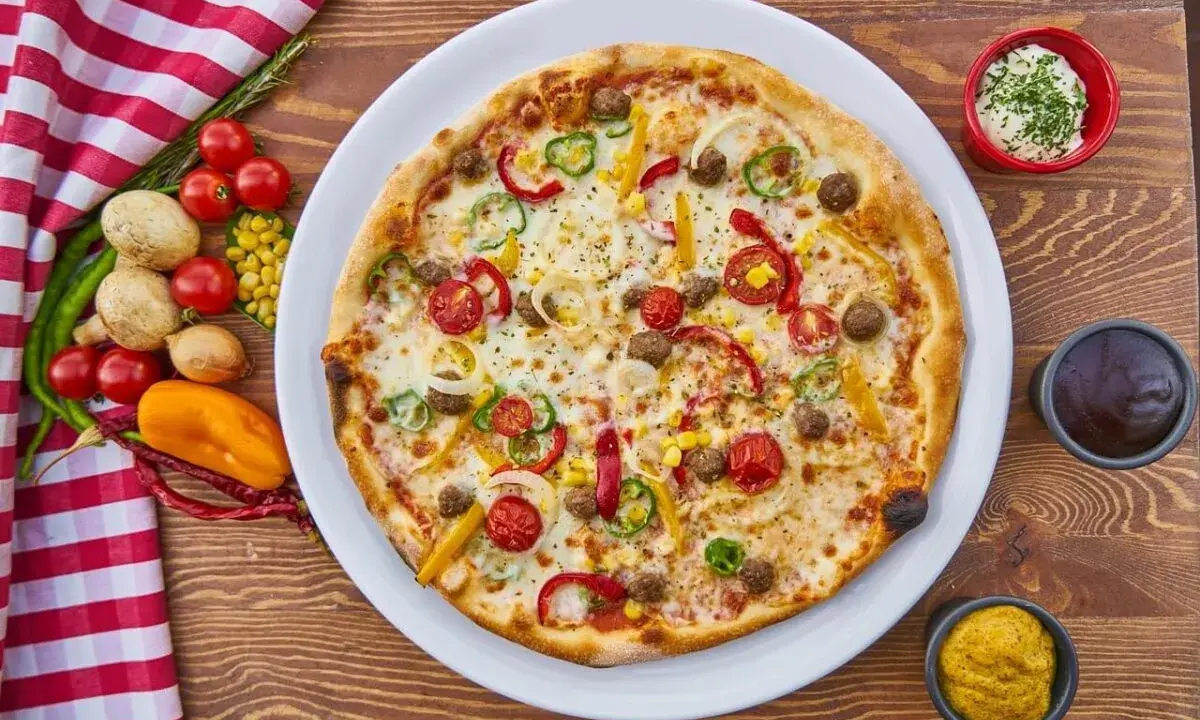 Pizza z mięsem mielonym, papryką, cebulą i kukurydzą. Obok sosy i warzywa, co zamiast śmietany?