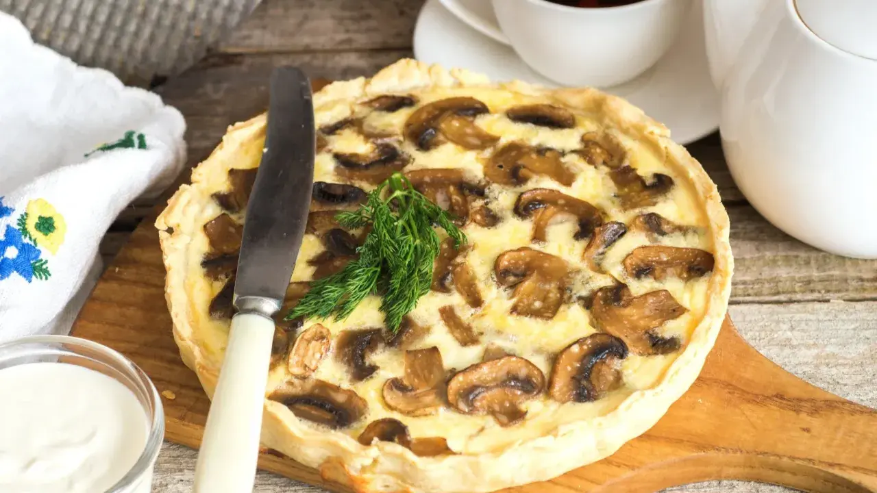 Pyszna tarta z pieczarkami, podana z kubkiem herbaty i śmietaną. Idealna na jesienny obiad.