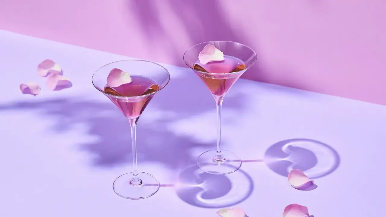 Dwa różowe drinki w kieliszkach do martini, ozdobione płatkami róż. Idealne co do martini na romantyczny wieczór.