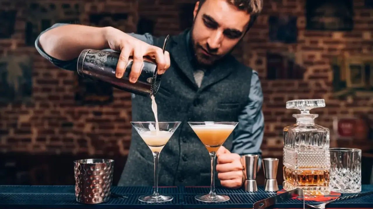 Barman przygotowuje drinki, zastanawiając się, jaki rum do mojito będzie najlepszy. Na blacie stoją kieliszki i karafka z bursztynowym płynem.