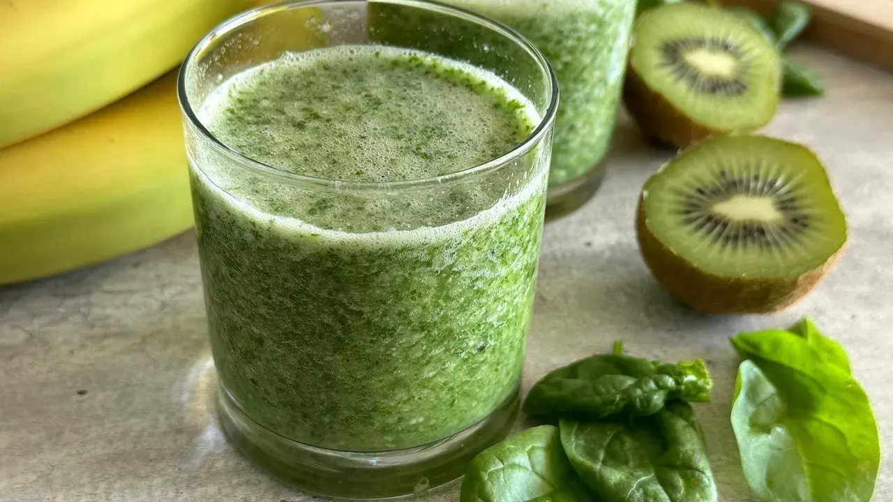 Orzeźwiający koktajl ze szpinakiem, bananami i kiwi. Zielony napój w szklance, obok świeże liście szpinaku i owoce.