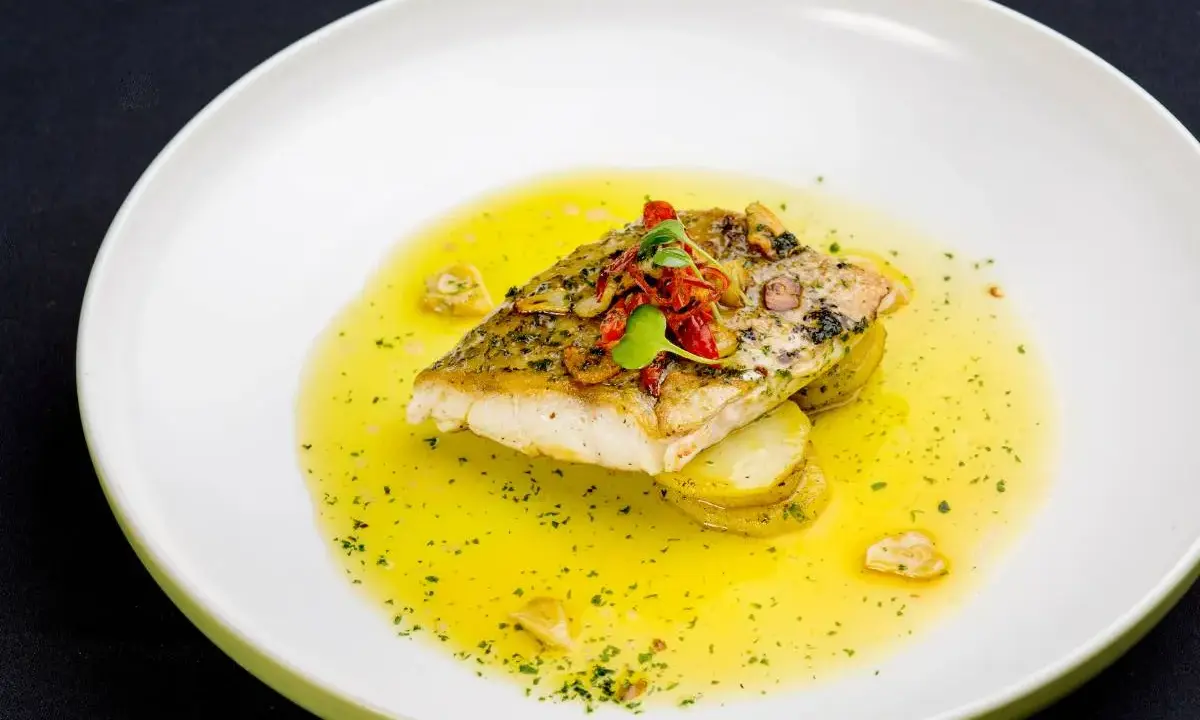 Filet ryby w aromatycznym sosie cytrynowym, podany na plastrach ziemniaków.
