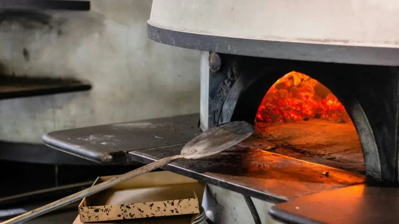 Piec do pizzy z rozżarzonymi węglami. Łopatka czeka, by włożyć do środka pizzę, która będzie piec się w 200 stopniach.