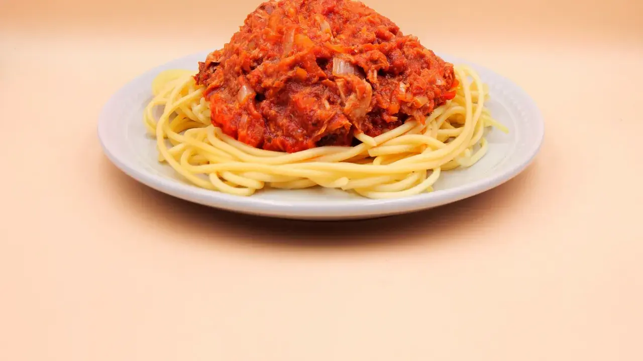 Porcja spaghetti z sosem pomidorowym i tuńczykiem, podana na jasnym talerzu.