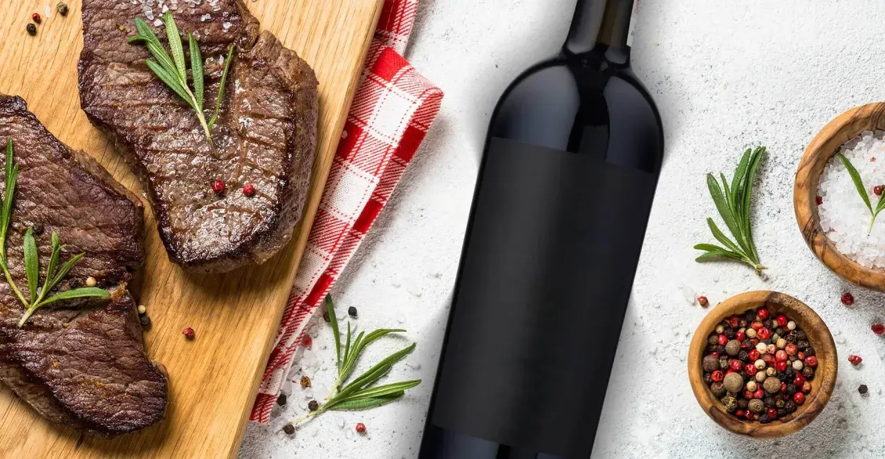 Idealne jakie wino do steka? Soczyste steki na desce, butelka czerwonego wina i przyprawy.