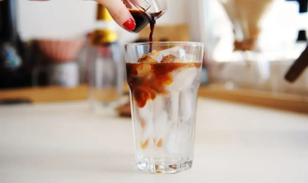 Ręka wylewa espresso na lód w szklance. Idealny napój na upalne dni - tonic espresso.