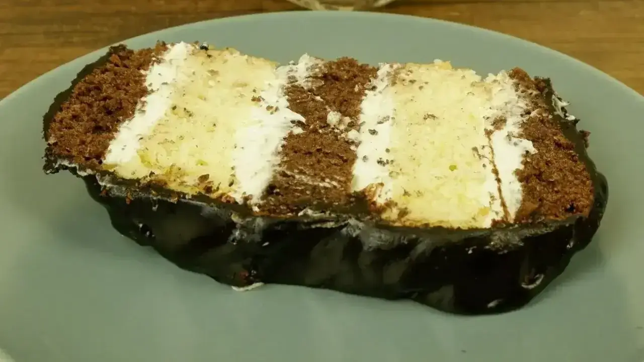 Kawałek ciasta z czekoladą i kremem budyniowym z mascarpone, polany błyszczącą polewą.
