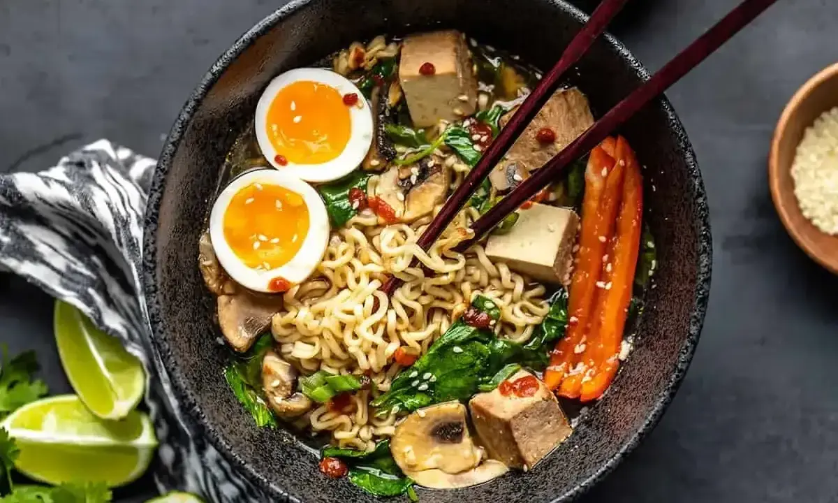 Miseczka ramenu z makaronem, jajkiem na pół, tofu, grzybami i szpinakiem. Dodatki do ramenu tworzą apetyczną całość.