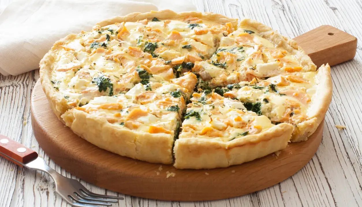 Pyszna tarta z łososiem, szpinakiem i serem feta, pokrojona na kawałki, czeka na talerzu.