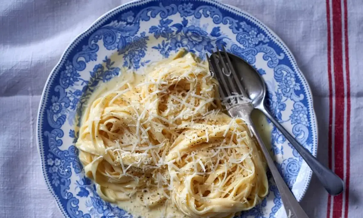 Pyszny makaron alfredo przepis na talerzu z widelcem i łyżką, posypany startym parmezanem.