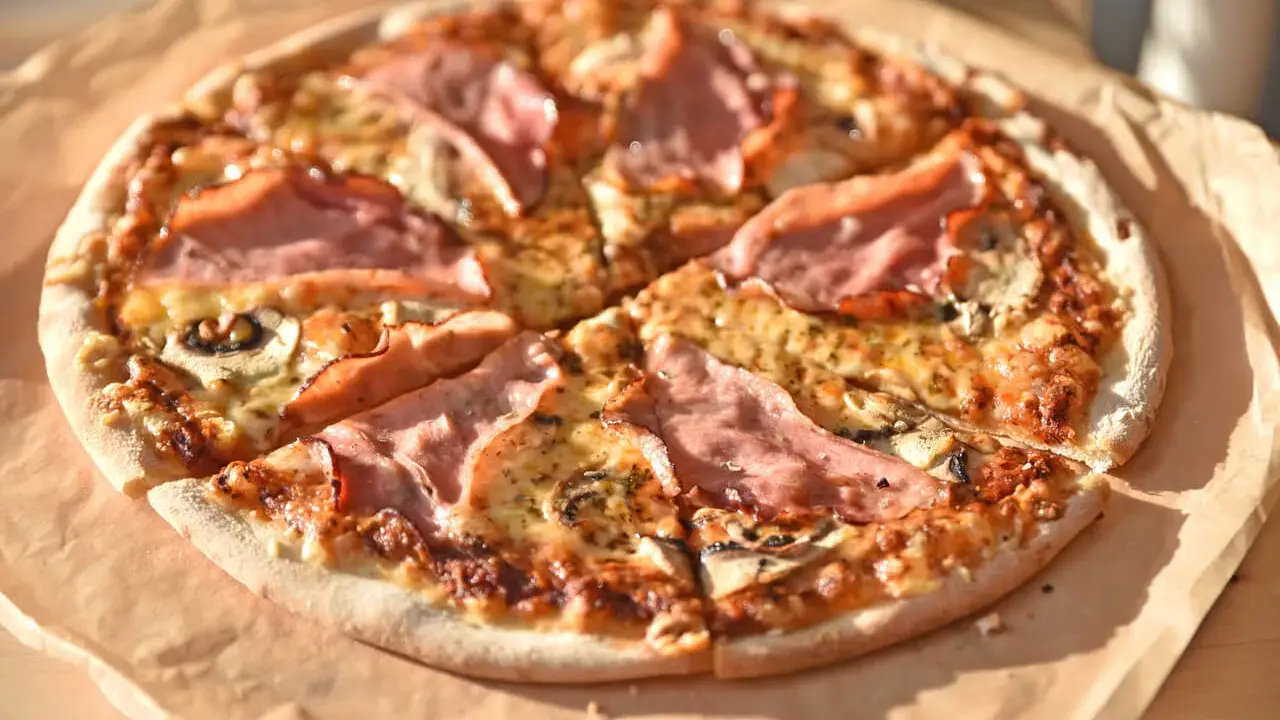 Pizza z szynką i pieczarkami do pizzy, pachnąca i apetyczna, gotowa do podania.