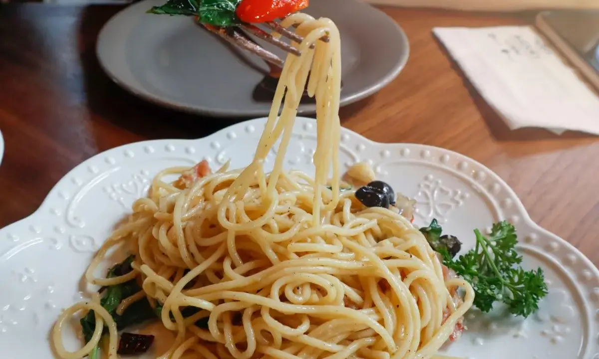Widok z bliska na talerz pysznego spaghetti aglio e olio, z widelcem unoszącym porcję makaronu, pomidorkiem i bazylią.