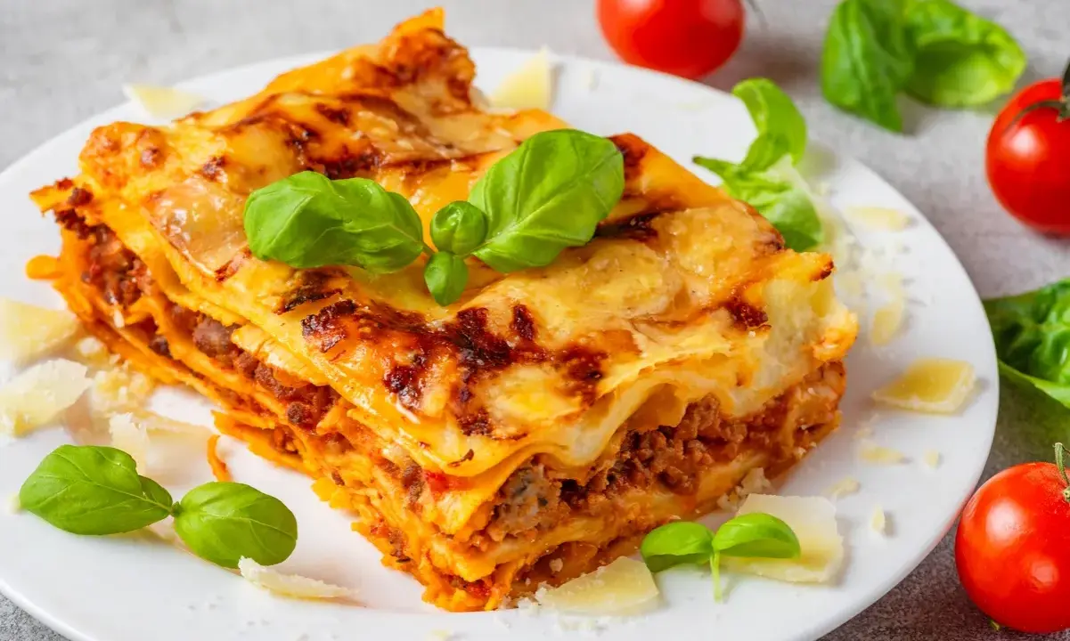 Pyszna, domowa lasagne jak z pieca, z warstwami makaronu, mięsa i sera, ozdobiona świeżą bazylią i parmezanem.