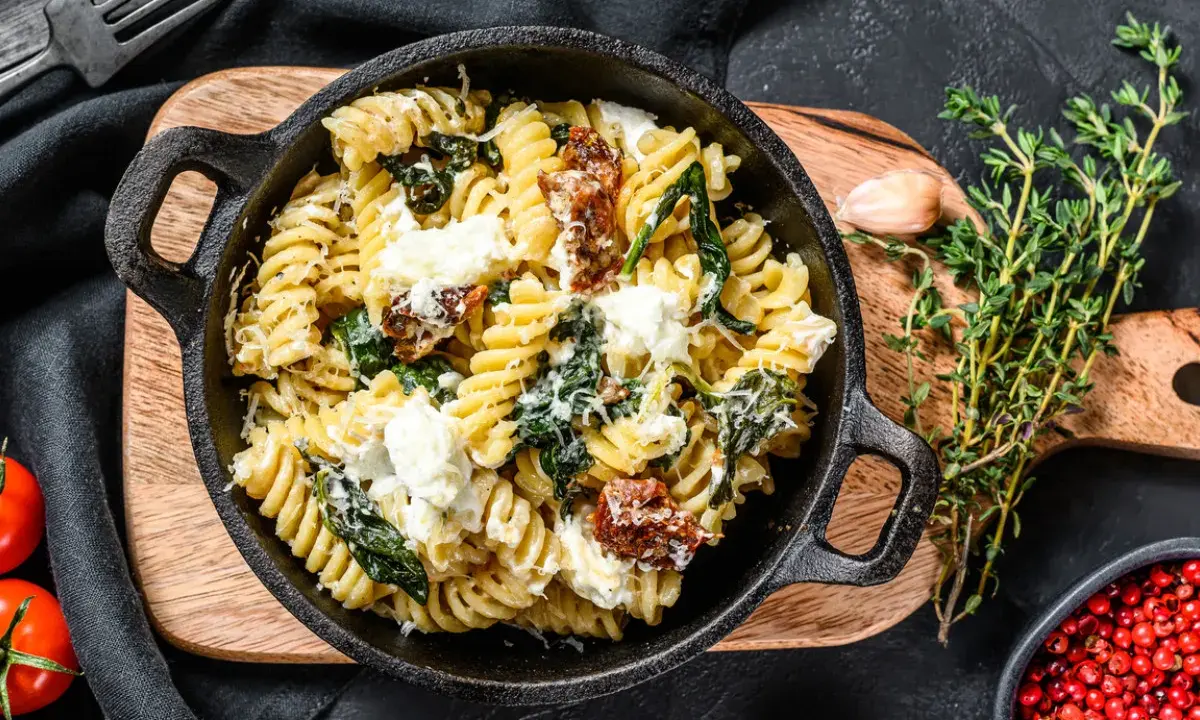 Pyszne fusilli ze szpinakiem i suszonymi pomidorami, posypane parmezanem i kawałkami sera feta.