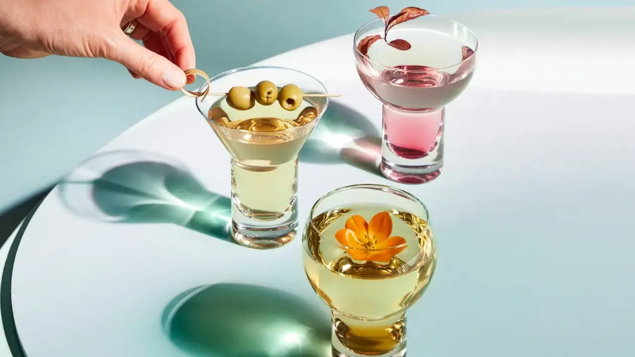 Eleganckie drinki z wódką: martini z oliwkami, różowy koktajl i złoty napój z kwiatem.