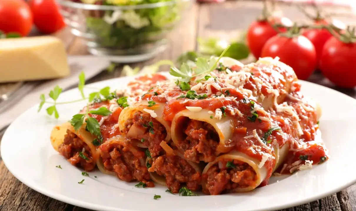 Pyszne cannelloni z mięsem mielonym, polane sosem pomidorowym i posypane parmezanem, na talerzu z pomidorami i sałatką.