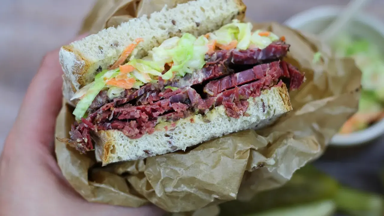 Pyszna kanapka z pastrami, z chrupiącą surówką i musztardą, zawinięta w papier.