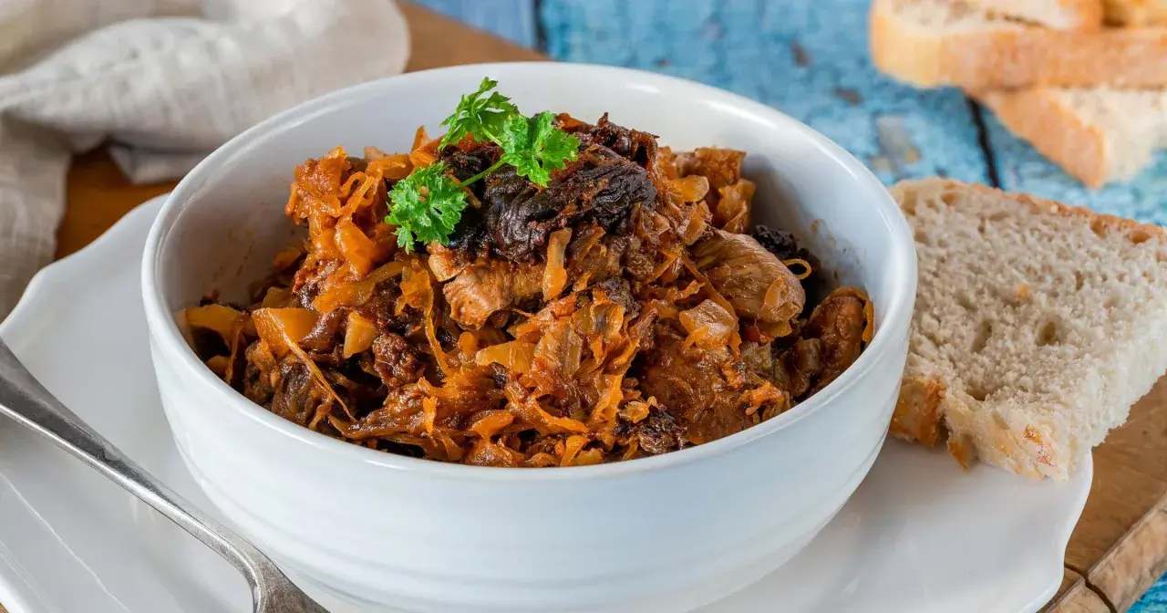 Pyszny bigos w białej misce, z gałązką natki pietruszki. Obok kromki chleba. Idealny na zimowe wieczory.
