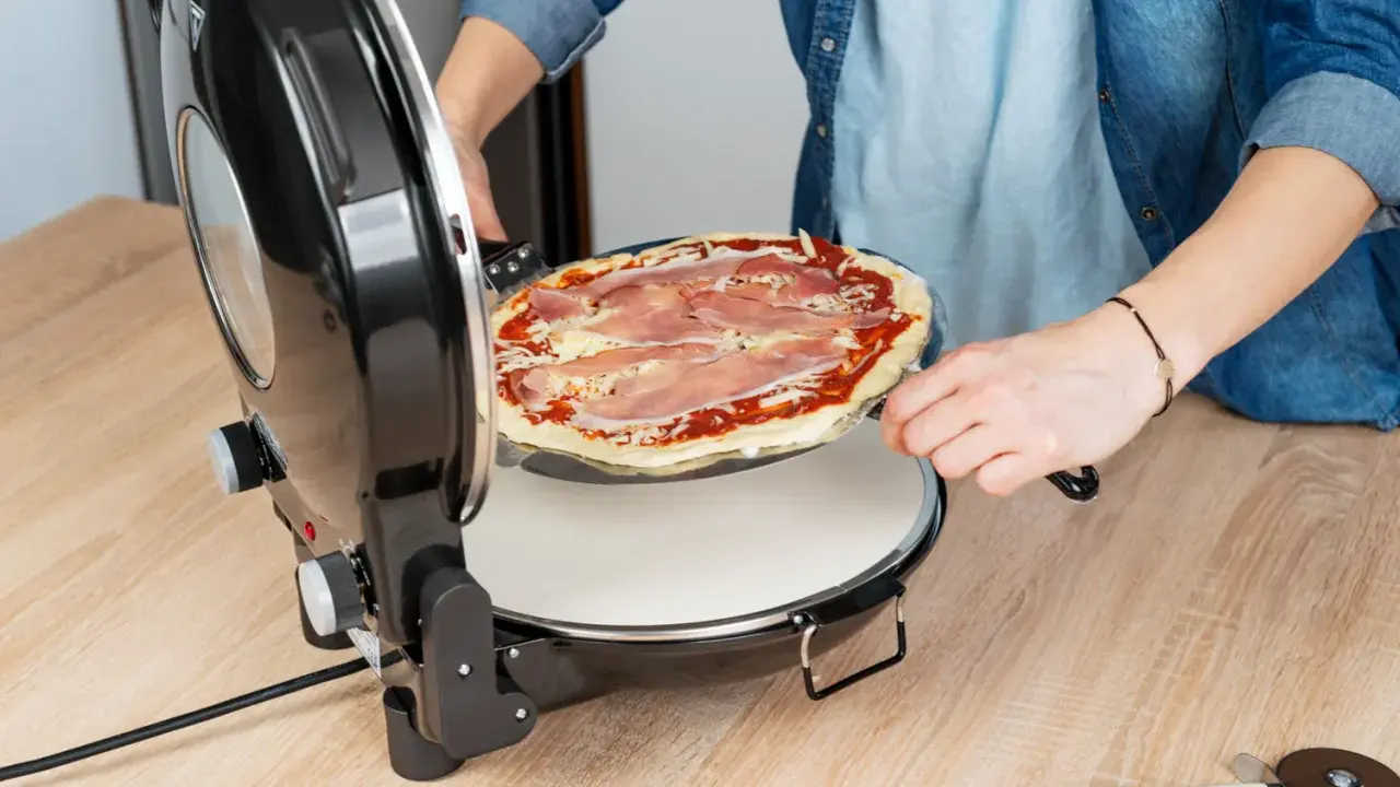 Osoba wkłada pizzę z szynką do okrągłego piekarnika. Idealny moment na pieczenie pizzy w piekarniku!