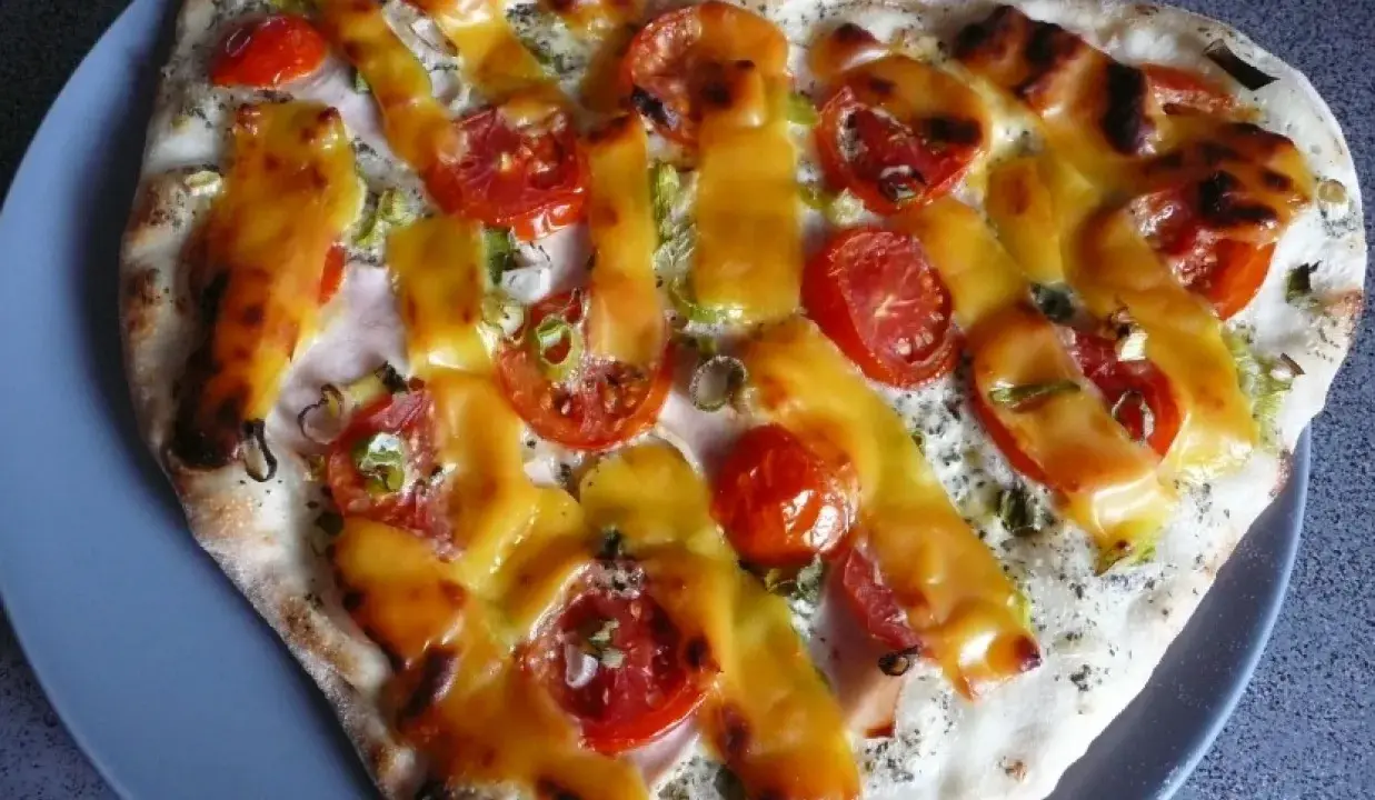 Pizza z pomidorami i serem, polana sosem śmietanowym.