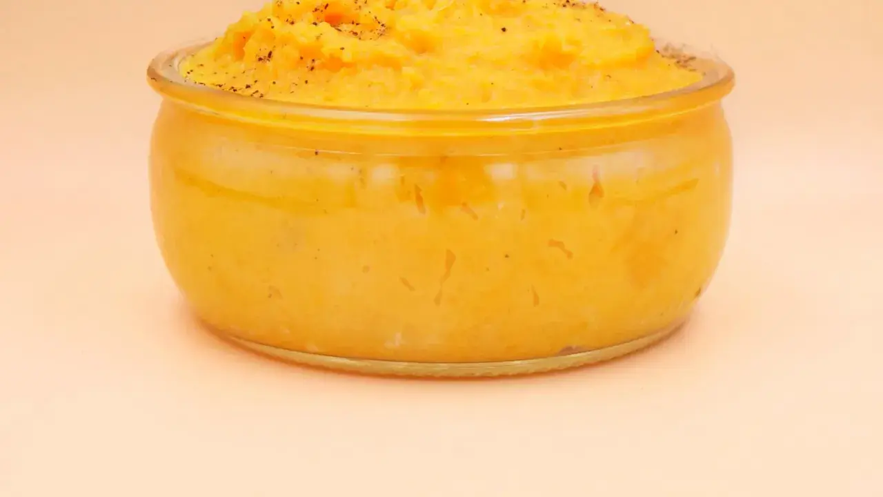 Pomarańczowe puree z batatów w szklanym naczyniu, posypane pieprzem.