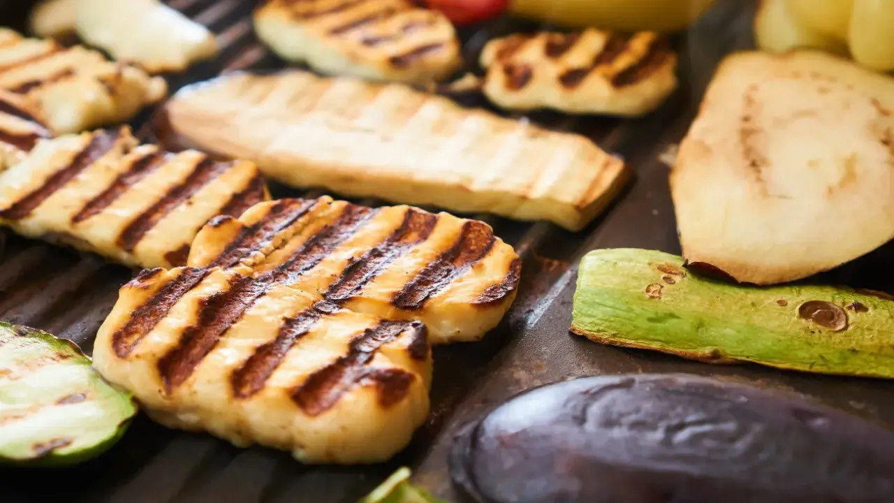 Grillowany ser halloumi z paskami od rusztu, obok cukinia, bakłażan i inne warzywa.