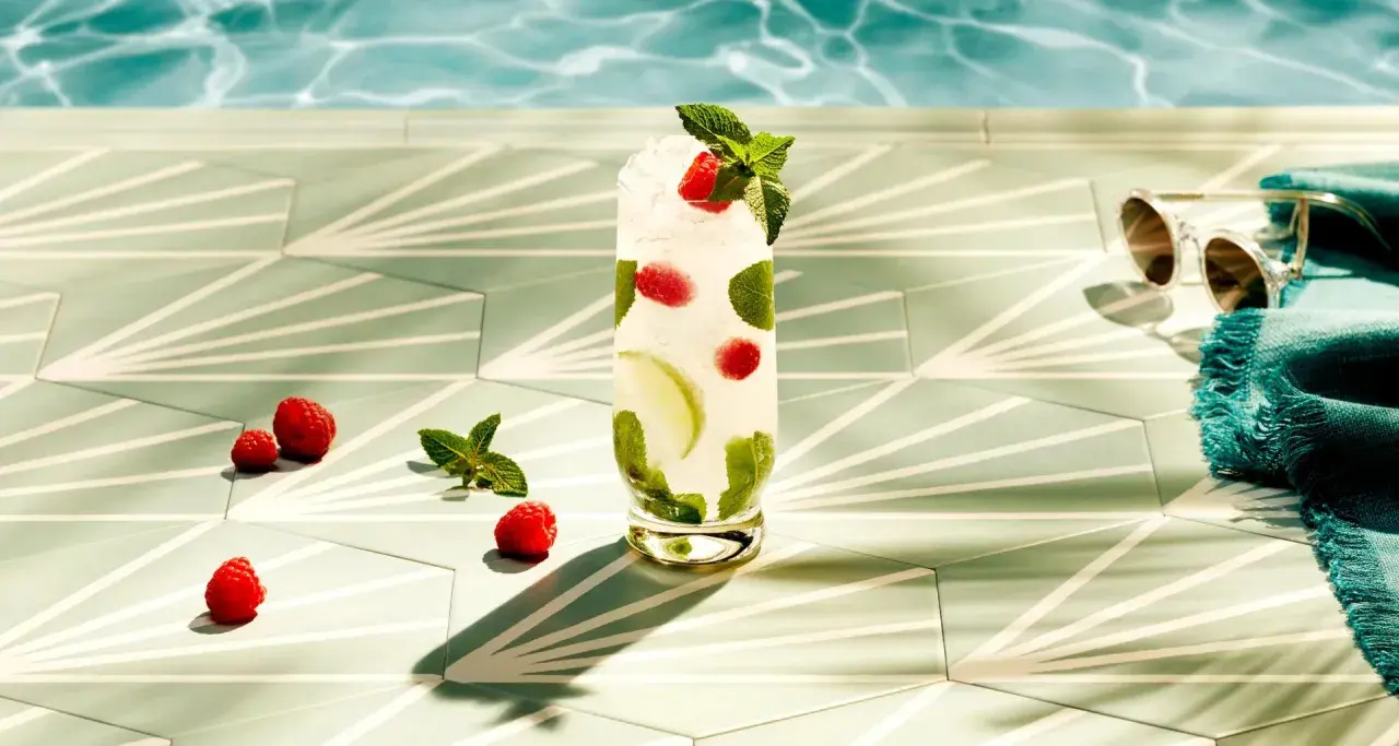 Orzeźwiający drink z malinami i miętą, idealny do Bacardi malinowego. Obok leżą maliny, a w tle widać basen i okulary przeciwsłoneczne.
