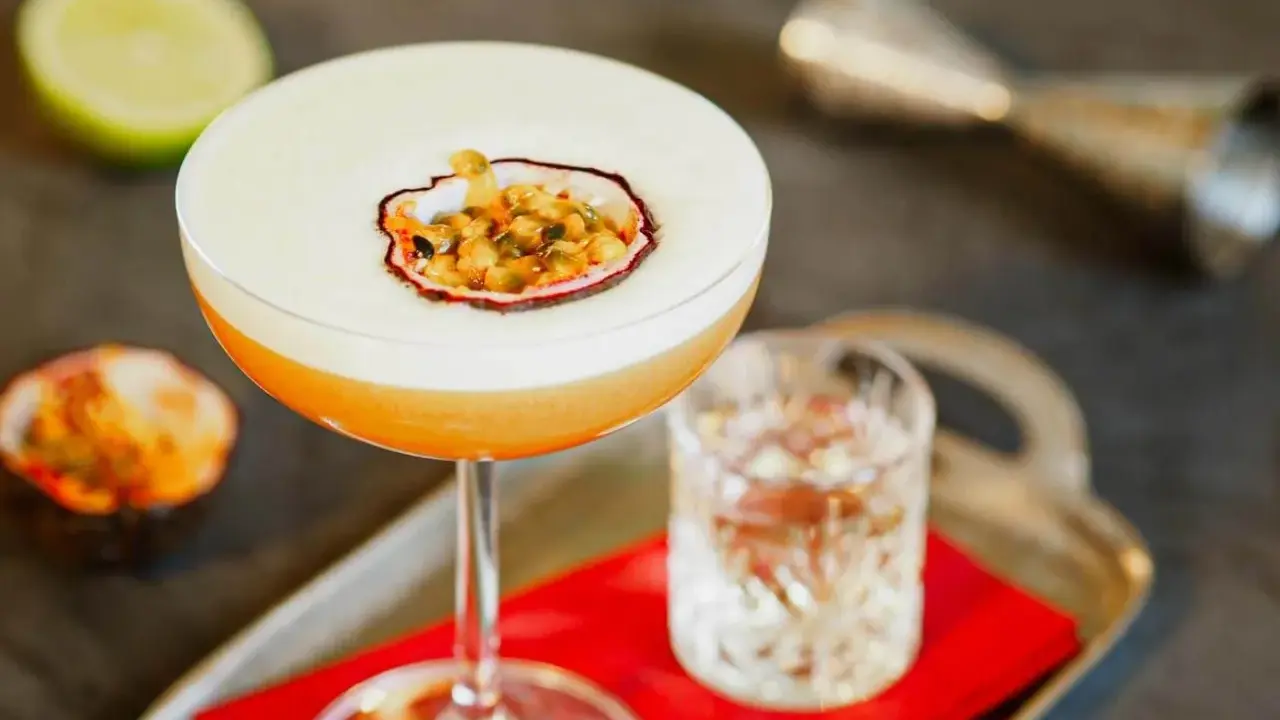 Pyszny drink Pornstar Martini z pianką i owocem marakui, obok kieliszek z drinkiem i połówka limonki.
