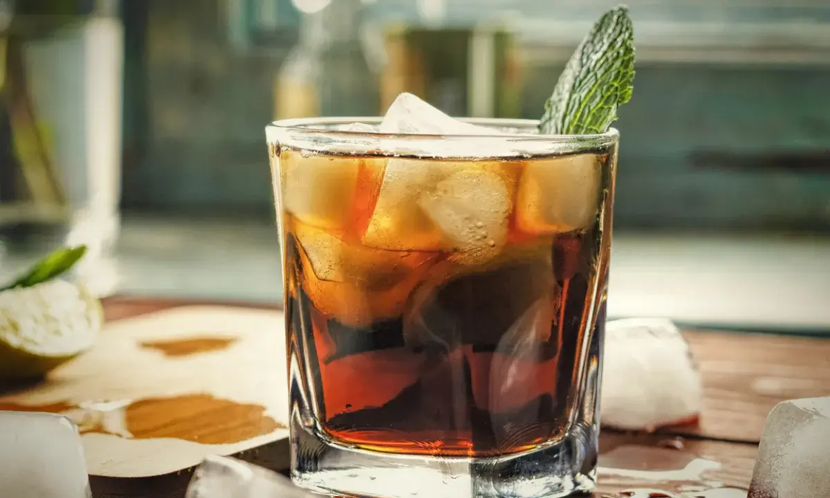 Orzeźwiający gin z colą, z lodem i listkiem mięty, na drewnianym blacie. Idealny na letnie popołudnie.