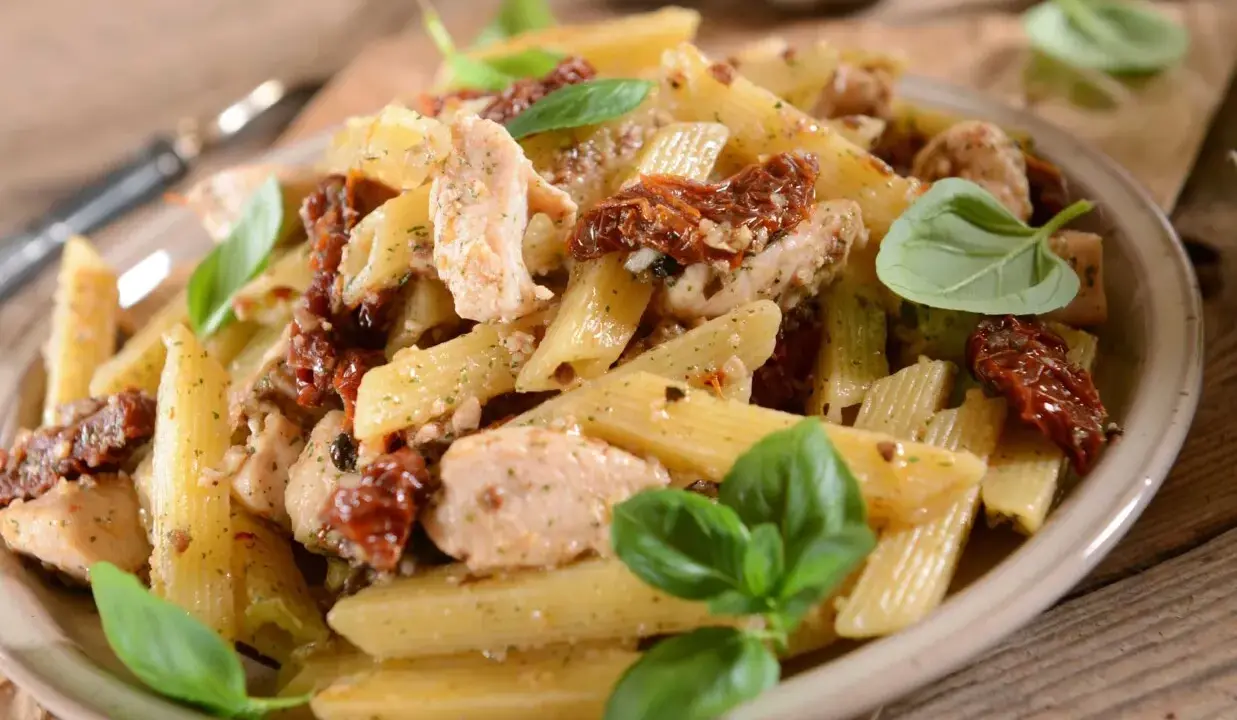 Penne z kurczakiem i suszonymi pomidorami, udekorowane świeżą bazylią. Pyszne danie na obiad.
