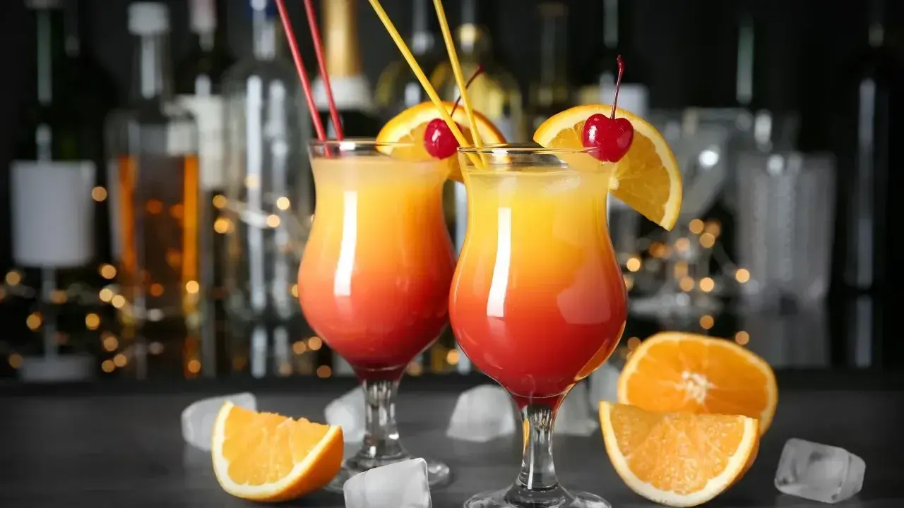 Dwa drinki z wódką, ozdobione pomarańczą i wiśnią, na tle barowych butelek. Idealne na letnie wieczory.