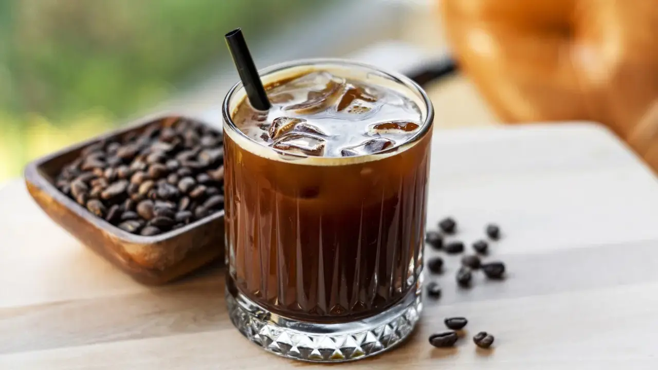Orzeźwiający cold brew z lodem i słomką, obok miseczka z ziarnami kawy. Idealny na gorący dzień.