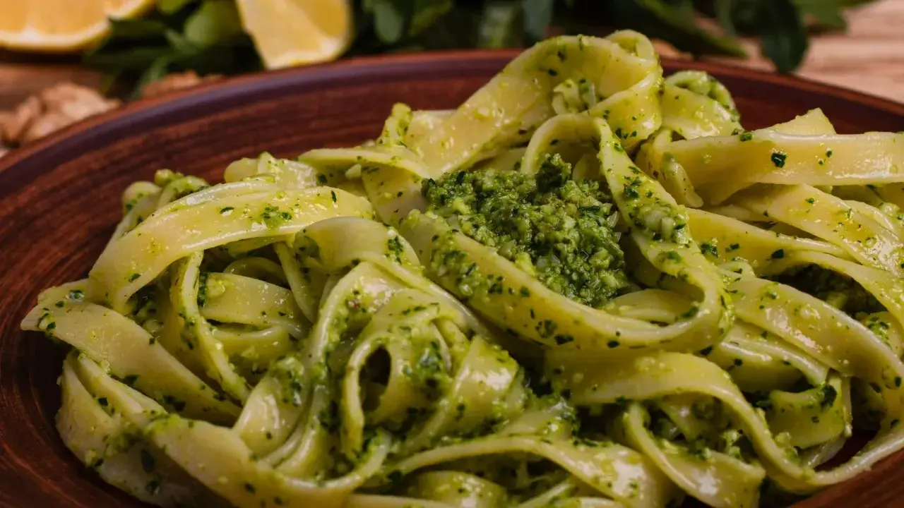 Pappardelle z aromatycznym makaronem z pesto, podane na glinianym talerzu. W tle cytryny i rukola.