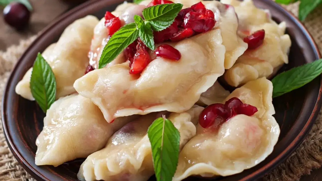 Pyszne, domowe ciasto na pierogi z wiśniami i miętą, podane na glinianym talerzu.