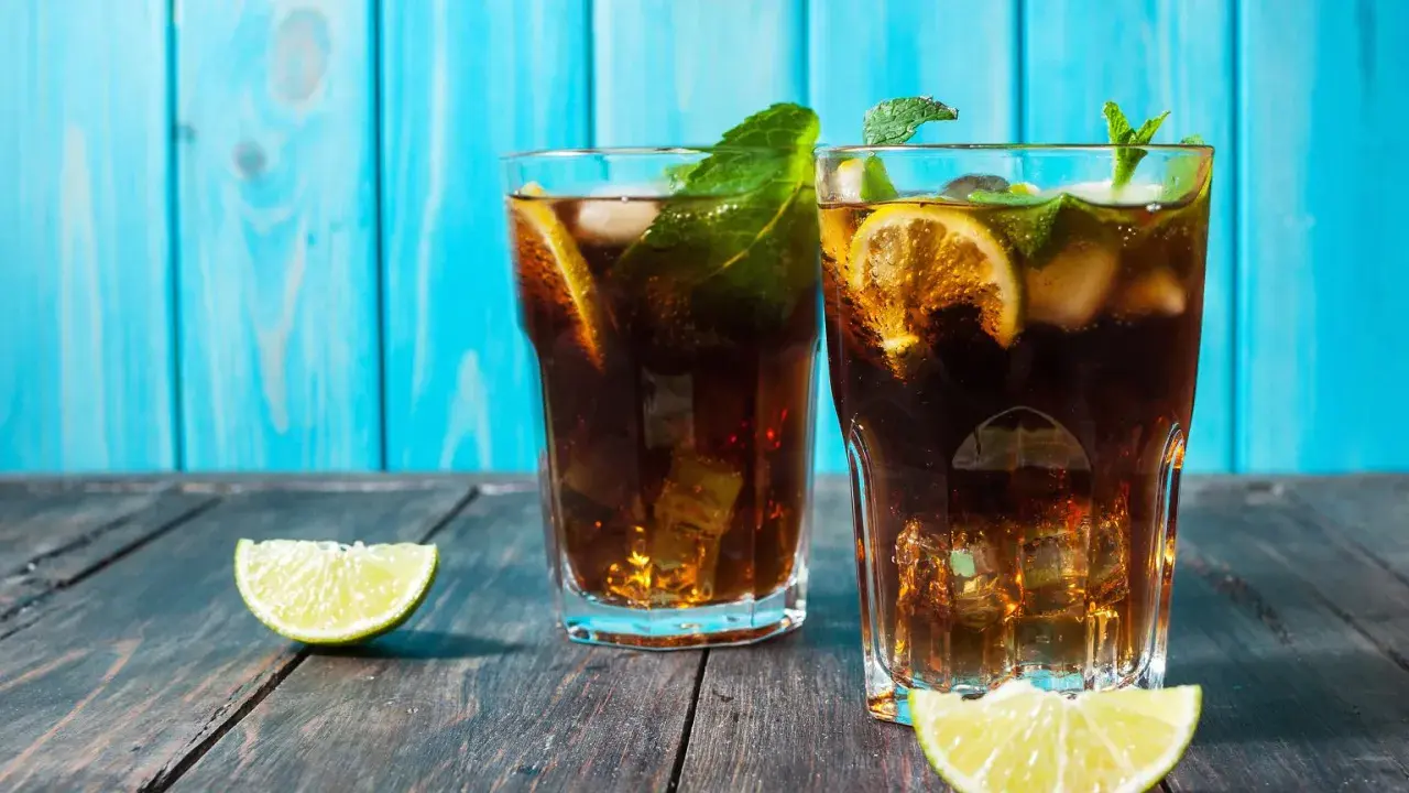 Dwa orzeźwiające drinki z rumem ciemnym, lodem, cytryną i miętą na drewnianym blacie.