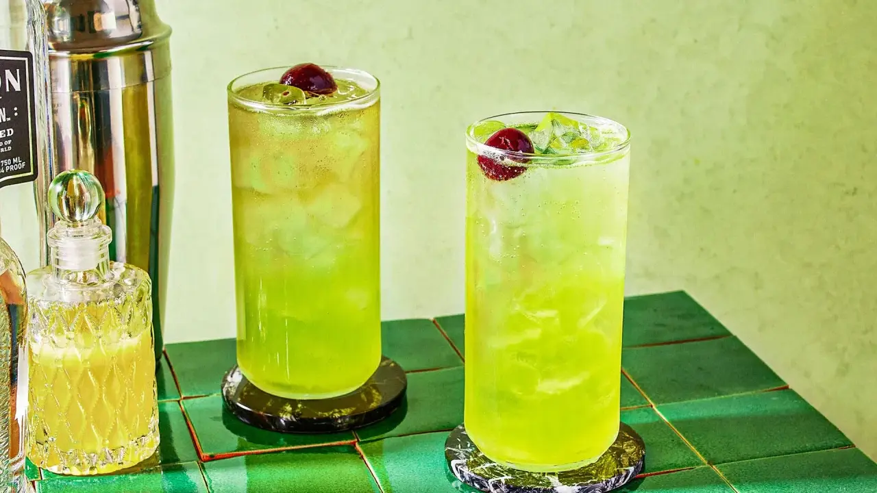 Dwa orzeźwiające drinki Tokyo Ice Tea z wiśniami i lodem, obok shakera i buteleczki z likierem.