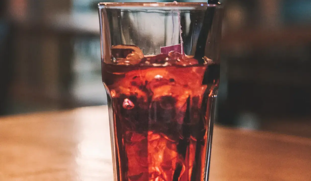 Szklanka z lodem i ciemnym napojem, idealne proporcje whisky z colą. Czarna słomka zanurzona w napoju.