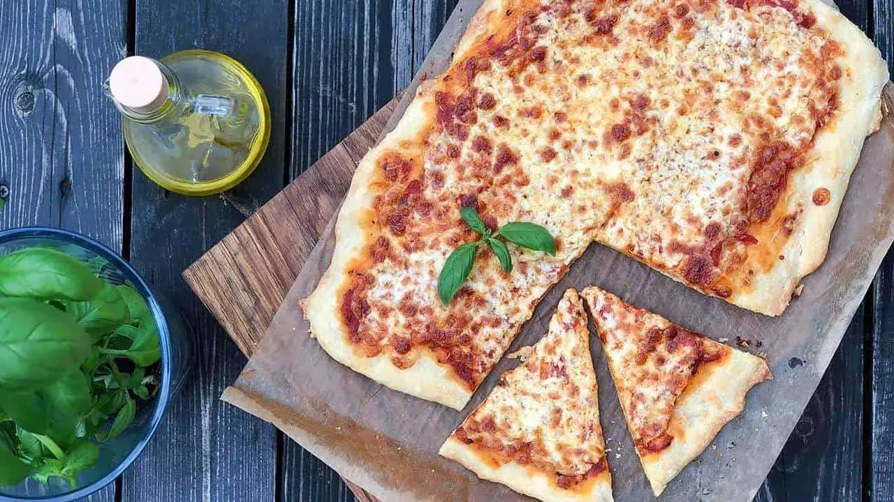 Pyszna pizza margherita z roztopionym serem i świeżą bazylią, obok butelka oliwy i miseczka ziół.